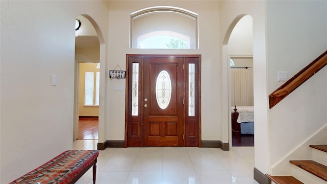 tiled foyer with baseboards, stairway, arched walkways, and a high ceiling