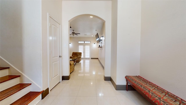 hall featuring light tile patterned flooring, arched walkways, stairs, and baseboards