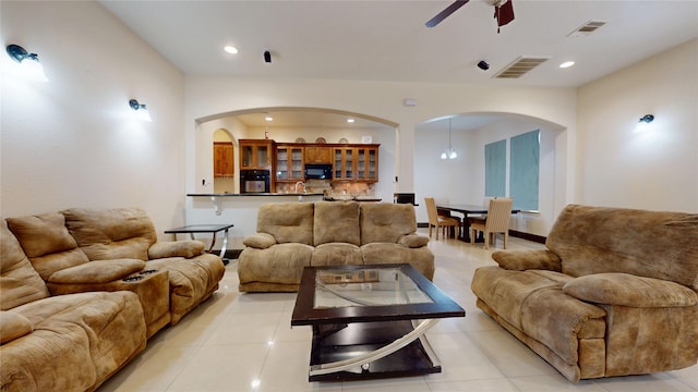 living room featuring light tile patterned flooring, visible vents, a ceiling fan, and arched walkways