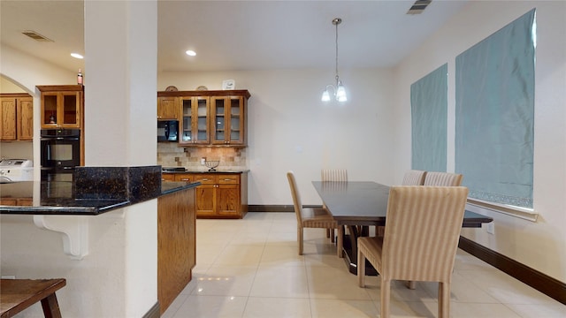 kitchen featuring brown cabinetry, tasteful backsplash, black microwave, visible vents, and arched walkways