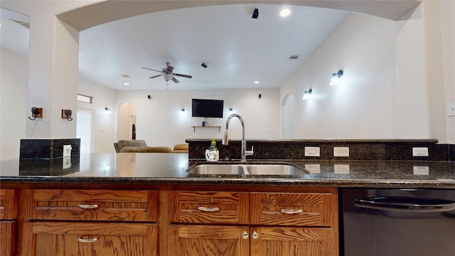 kitchen with arched walkways, dark stone counters, dishwasher, a sink, and a ceiling fan