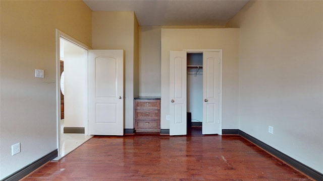 unfurnished bedroom with dark wood-style flooring, a closet, and baseboards