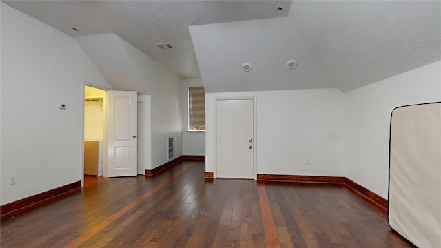 interior space featuring wood-type flooring, visible vents, lofted ceiling, and baseboards