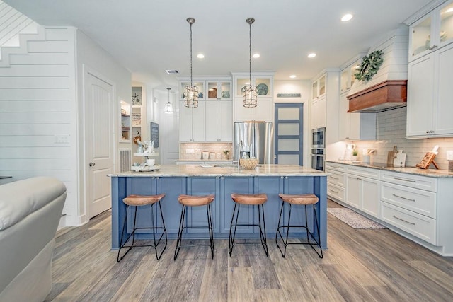 4110 Defender Ln, Galveston, TX 77554 - kitchen featuring custom exhaust hood, decorative backsplash, stainless steel appliances, white cabinetry, and light wood-type flooring