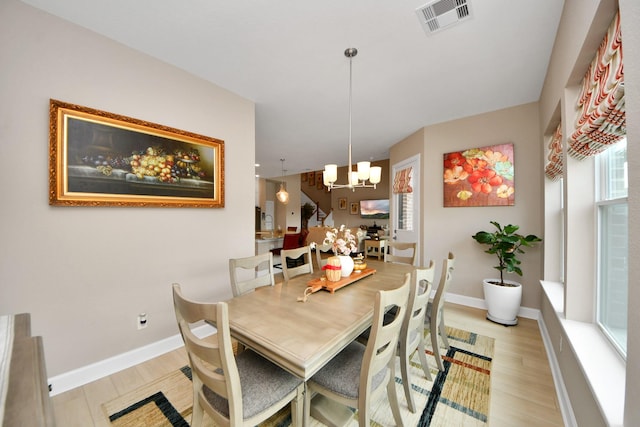 dining space with baseboards, light wood-type flooring, a chandelier, and visible vents