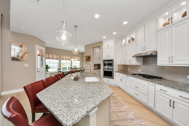 kitchen featuring a breakfast bar, under cabinet range hood, tasteful backsplash, a sink, and appliances with stainless steel finishes
