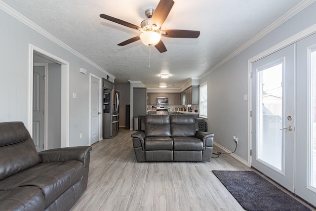 living area featuring baseboards, ceiling fan, light wood-style floors, and crown molding