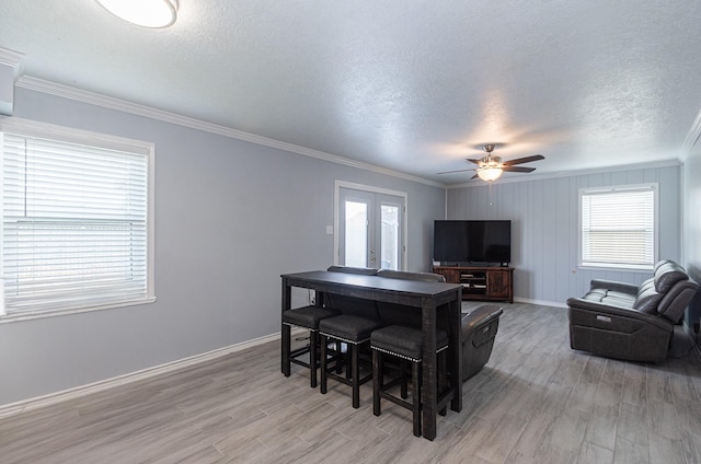 living room with a textured ceiling, light wood-style floors, ceiling fan, baseboards, and ornamental molding