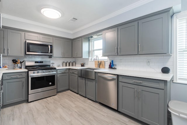 kitchen featuring gray cabinets, stainless steel appliances, backsplash, and crown molding