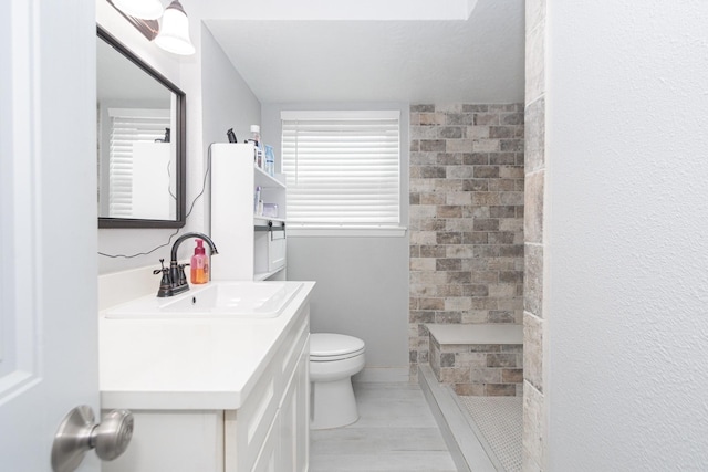 bathroom with a tile shower, toilet, and vanity