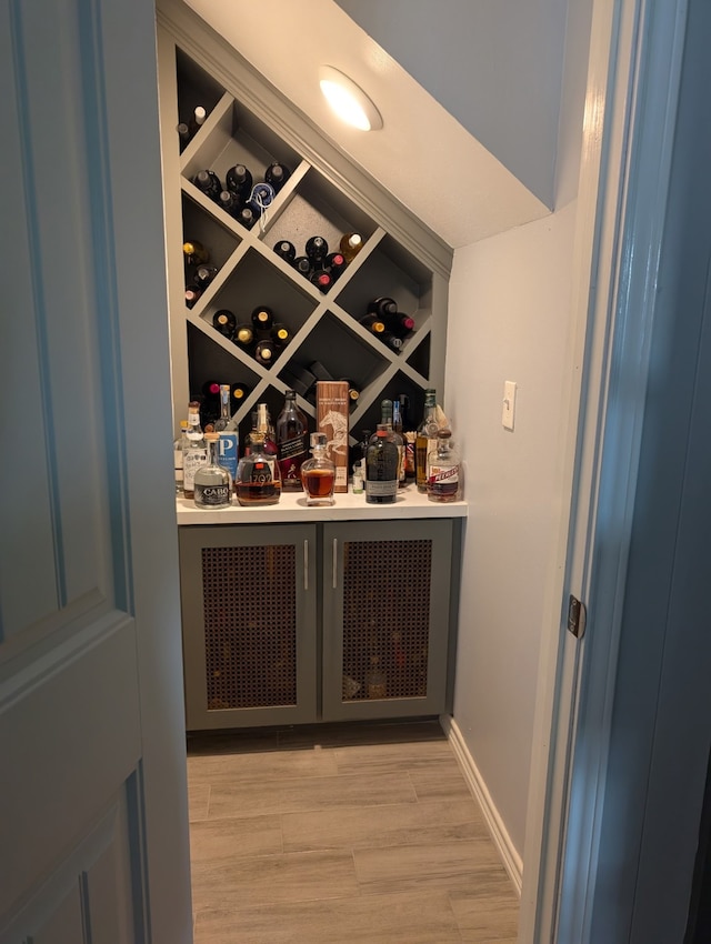 wine room with baseboards, a bar, and light wood-style floors