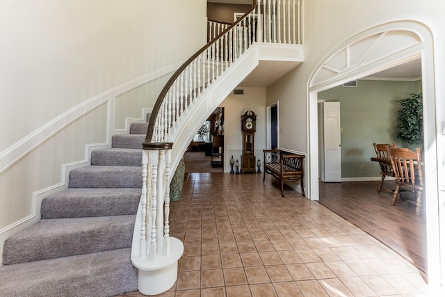 staircase featuring a towering ceiling, visible vents, and ornamental molding
