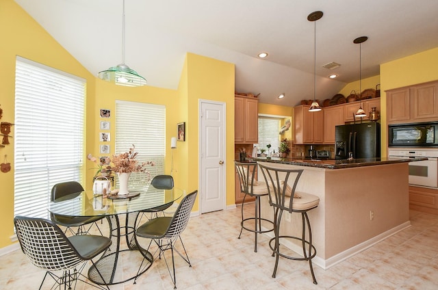 kitchen with a breakfast bar area, vaulted ceiling, black appliances, dark countertops, and visible vents