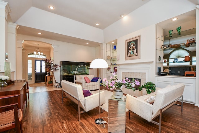 living area with a chandelier, ornate columns, a tiled fireplace, and dark wood finished floors