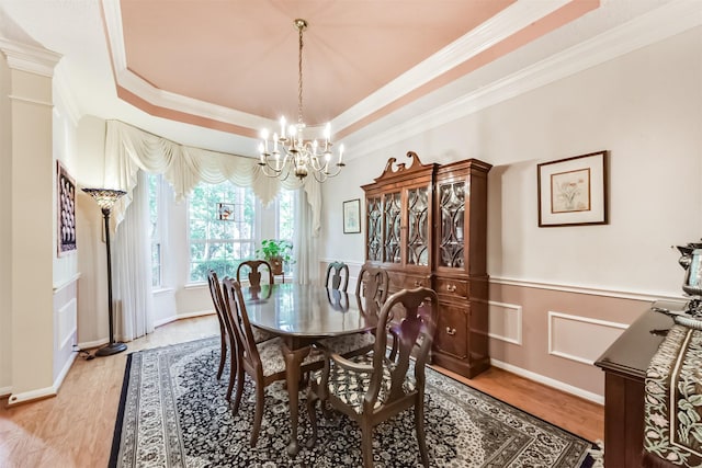 dining room with wainscoting, a raised ceiling, light wood finished floors, a notable chandelier, and ornamental molding