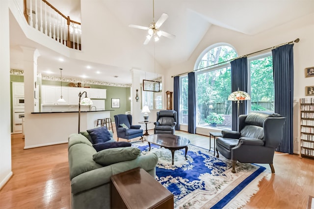 living room featuring baseboards, a ceiling fan, light wood finished floors, and high vaulted ceiling
