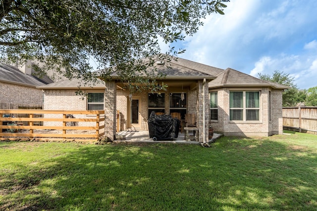 back of property with roof with shingles, a patio area, brick siding, a fenced backyard, and a yard