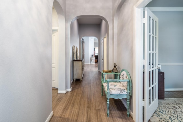 corridor featuring baseboards, arched walkways, and wood finished floors