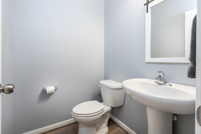 half bath featuring baseboards, wood finished floors, and toilet