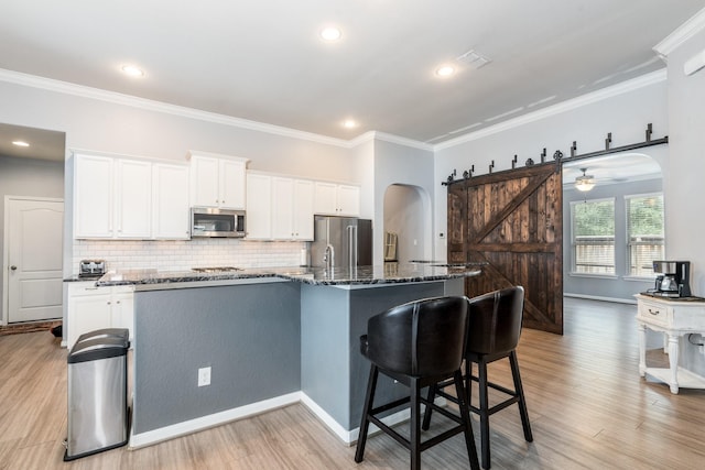 kitchen with a barn door, appliances with stainless steel finishes, white cabinets, and tasteful backsplash