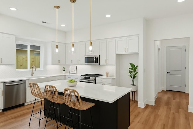 kitchen featuring appliances with stainless steel finishes, light wood-style floors, decorative backsplash, and white cabinetry