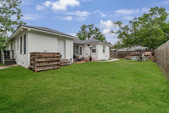 rear view of property with brick siding, roof with shingles, a fenced backyard, and a lawn
