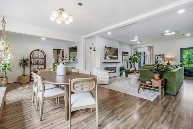 dining space with recessed lighting, a chandelier, a glass covered fireplace, visible vents, and wood finished floors