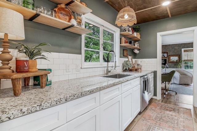 kitchen with open shelves, white cabinets, light wood-style flooring, a sink, and light stone countertops