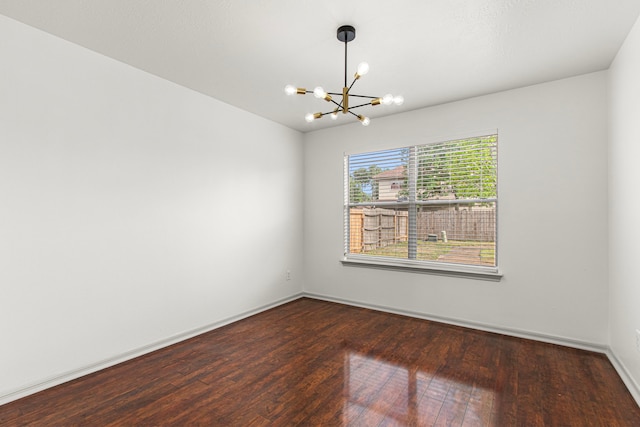 unfurnished room with a chandelier, baseboards, and dark wood-type flooring