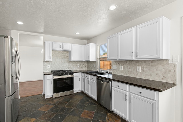 kitchen featuring dark countertops, stainless steel appliances, white cabinetry, and a sink