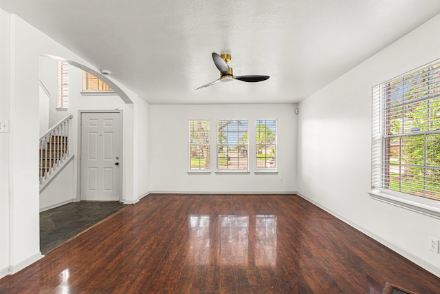 unfurnished living room with stairway, a ceiling fan, baseboards, arched walkways, and hardwood / wood-style floors