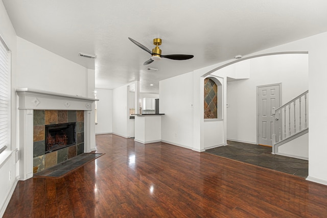 unfurnished living room with ceiling fan, visible vents, baseboards, a tile fireplace, and stairs