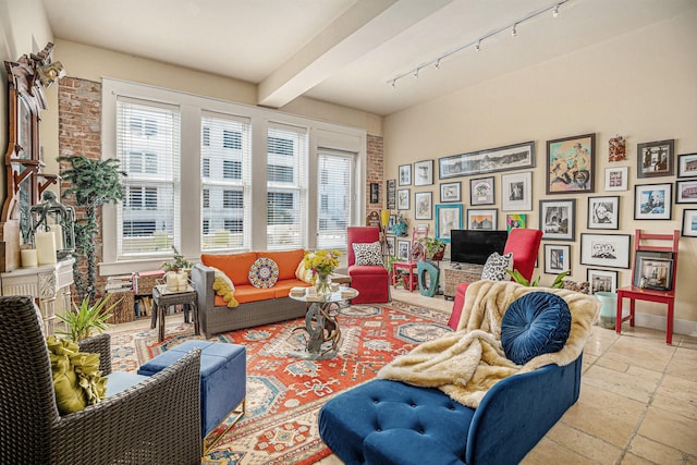 living room featuring track lighting, baseboards, stone tile flooring, and beamed ceiling