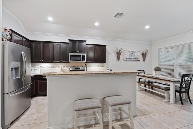 kitchen featuring appliances with stainless steel finishes, tasteful backsplash, ornamental molding, light tile patterned flooring, and a center island with sink