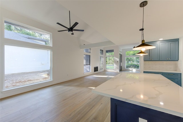kitchen featuring light stone counters, light wood-style flooring, ceiling fan, open floor plan, and hanging light fixtures