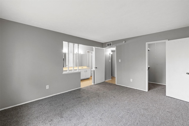 unfurnished bedroom with baseboards, ensuite bath, light colored carpet, a walk in closet, and visible vents