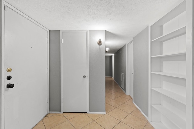 corridor with a textured ceiling, light tile patterned floors, baseboards, and built in shelves