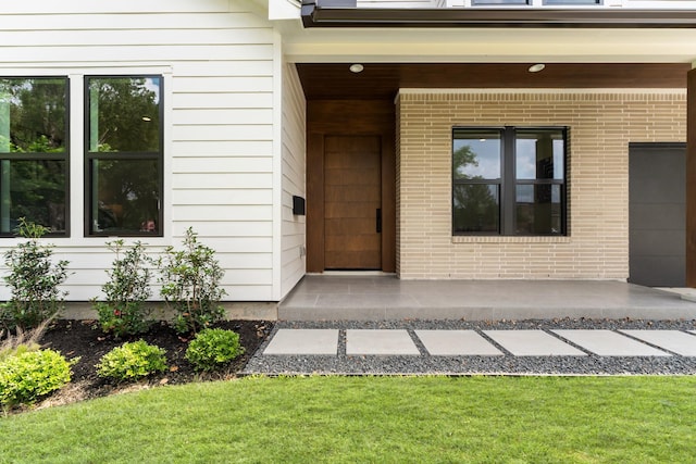 view of exterior entry with brick siding and a lawn