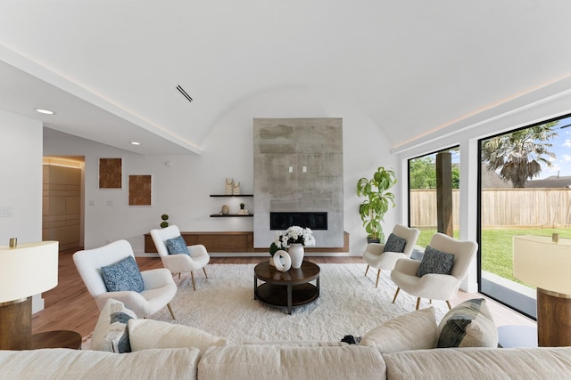 living area featuring vaulted ceiling, wood finished floors, visible vents, and a fireplace