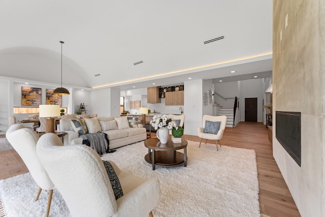 living room featuring high vaulted ceiling, stairway, recessed lighting, a large fireplace, and light wood-style flooring