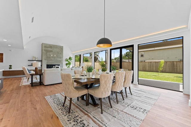 dining room featuring high vaulted ceiling, recessed lighting, light wood-type flooring, a tile fireplace, and visible vents