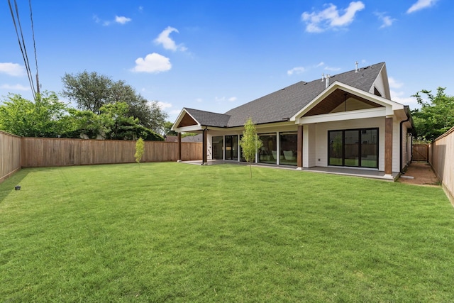 back of house with a fenced backyard, a patio, a shingled roof, and a lawn