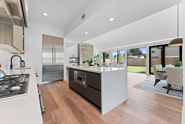 kitchen with a center island, modern cabinets, open floor plan, built in appliances, and light wood-style flooring