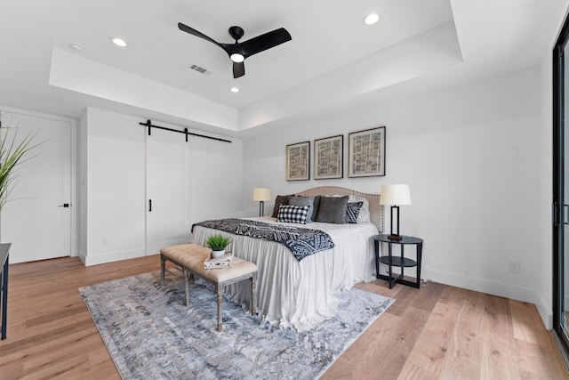 bedroom featuring visible vents, a barn door, baseboards, a tray ceiling, and light wood-style flooring
