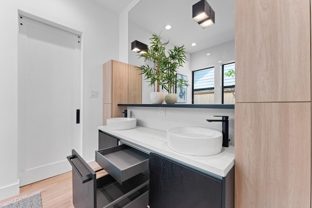 bathroom with a sink, double vanity, recessed lighting, and wood finished floors