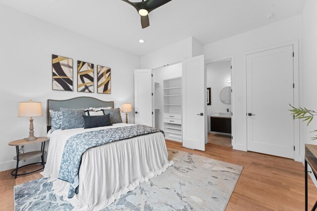 bedroom with a walk in closet, a ceiling fan, baseboards, wood finished floors, and ensuite bathroom