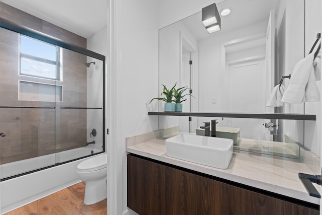 full bathroom featuring toilet, wood finished floors, shower / bath combination with glass door, and vanity