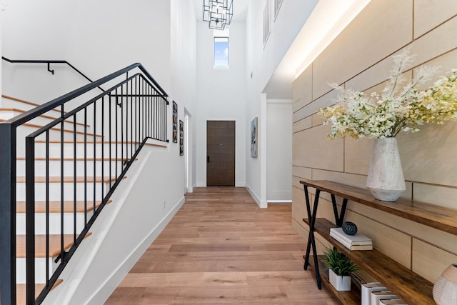 entryway with baseboards, light wood-type flooring, stairs, and a towering ceiling