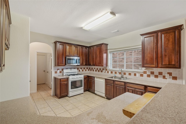 kitchen featuring decorative backsplash, a sink, light countertops, arched walkways, and white appliances