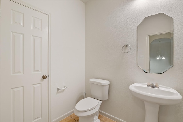 half bathroom featuring tile patterned floors, baseboards, toilet, and a sink